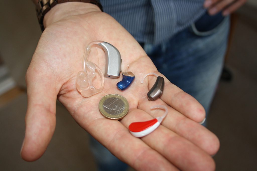 Plusieurs appareils auditifs posés dans une main à côté d'1 euro