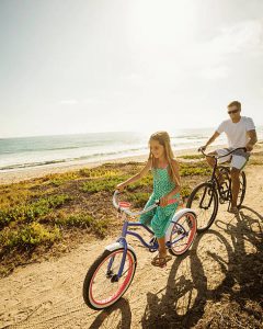 Père et sa fille en train de faire du vélo le long de l'océan