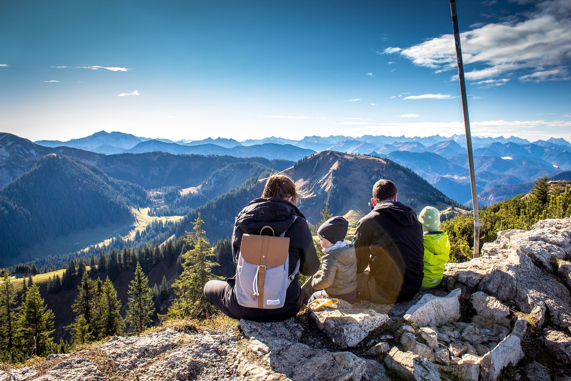 Vue de dos d'une famille qui est assise tout en haut d'une falaise et qui regarde le panorama